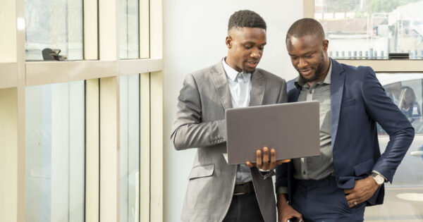 Young black businessmen standing together holding a laptop, discussing business Two young black businessmen standing together holding a laptop, discussing business